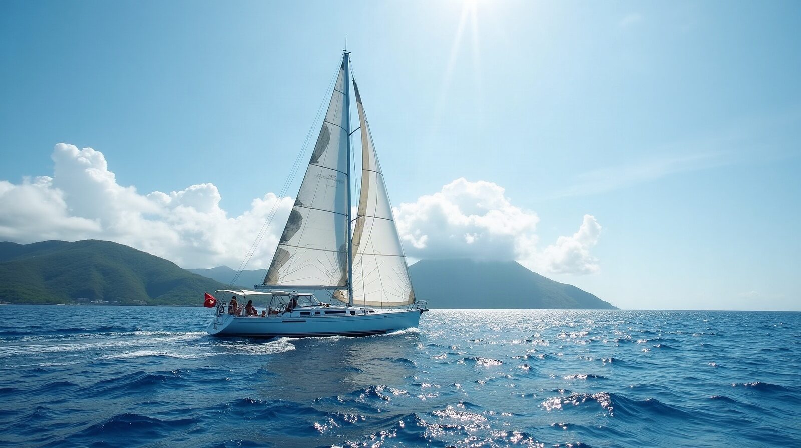 Un voilier de course toutes voiles dehors approche d'une baie antillaise, vu depuis la côte rocheuse.